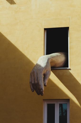 A vertical shot of a yellow building with a statue of a hand coming out of a window