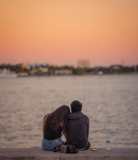 A closeup of a couple from behind sitting on the coastline at sunset