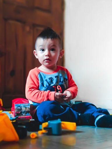 A selective focus shot of a cute baby boy with a curious face sitting on the floor around toys