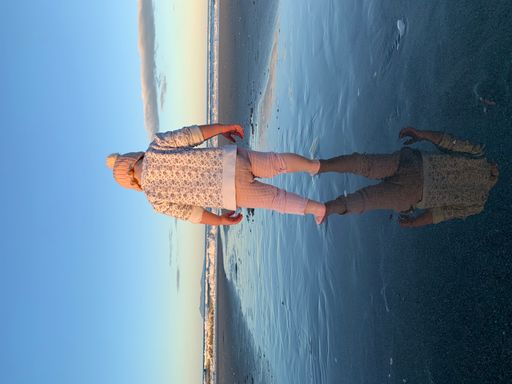 A vertical shot of a child standing on the beach with her reflection in the water