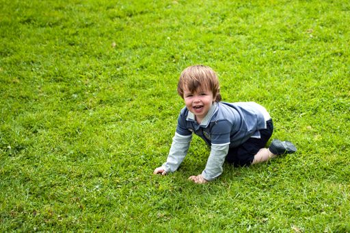 A cute little smiling male baby playing outdoors on a green lawn