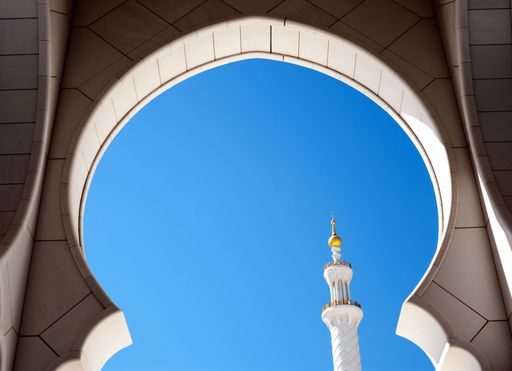 A keyhole arch of the Sheikh Zayed Grand Mosque in Abu Dhabi against a clear blue sky