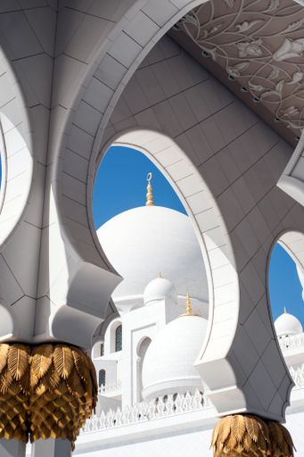A vertical shot of the domes of Sheikh Zayed Grand Mosque against a clear blue sky in Abu Dhabi