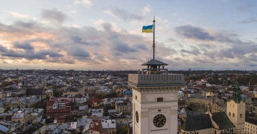 A horizontal shot of the flag of Ukraine on a flagpole on a clock tower surrounded by buildings in Lviv, Ukraine
