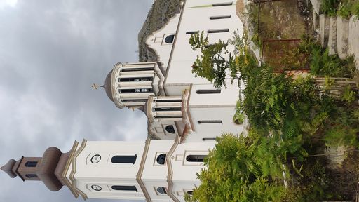 A vertical shot of the Bosnian Orthodox church hidden behind the trees under a cloudy sky