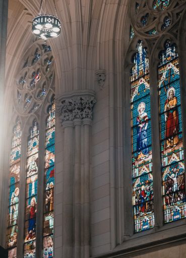 A vertical shot of the interior of a church with gray walls and mosaic paintings of religious saints on windows