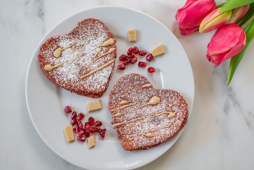 A top view of heart pancakes with pomegranates on a plate on a table