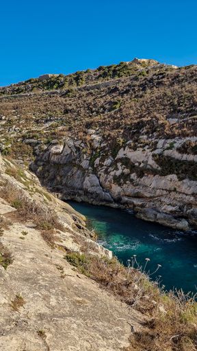 A vertical shot of a river flowing between the rocks under the clean sky