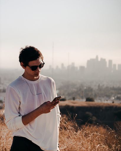 A vertical shot of a male with a smartphone outside and a city buildings in a distance