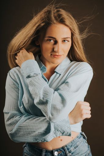 A vertical shot of an attractive blonde female in jeans and a short shirt posing on a brown background