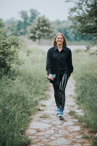 A vertical shot of a smiling young caucasian fashionable blonde female walking through a path