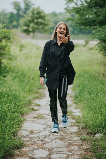 A vertical shot of a smiling young caucasian fashionable blonde female walking through a path
