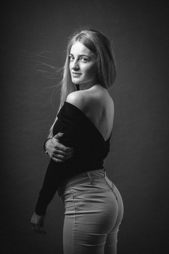 A vertical greyscale shot of an attractive blonde female posing while sitting on a barstool