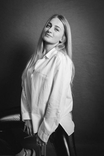 A vertical greyscale shot of an attractive blonde female posing while sitting on a barstool
