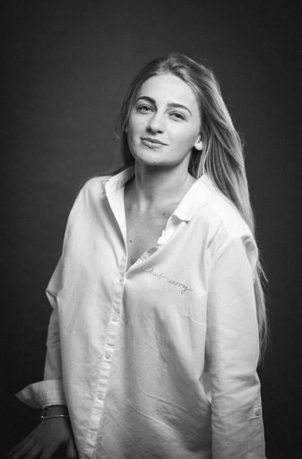 A greyscale shot of an attractive caucasian blonde female in a white shirt posing on a brown background