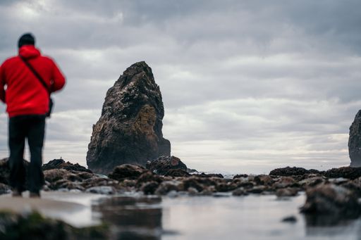 A beautiful shot of a male standing near a rock formation at the coast of the sea