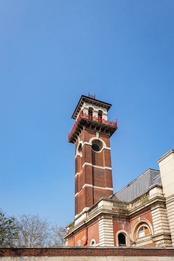 A vertical shot of brick clock tower in London against a blue background
