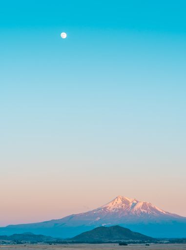 A beautiful aesthetic shot of a snowy mountain and the moon in the clear blue amazing sky