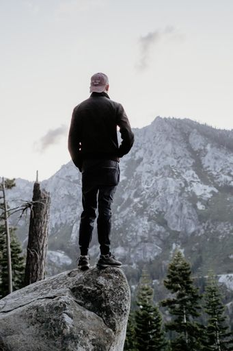 A male in a warm coat standing on a rock in a forest near the edge of a cliff