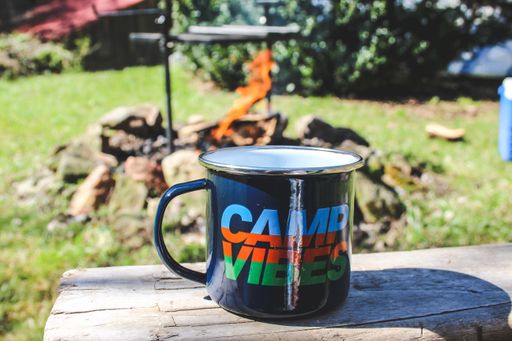 A selective closeup shot of a black metal cup with "camp vibes" writing on background of fire in nature