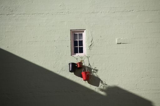 A closeup shot of a cute small window with three plant pots hanging on it under the sun