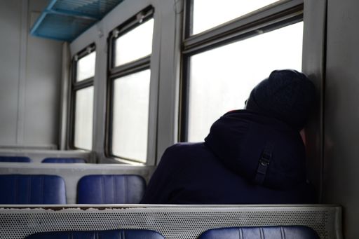A lonely passenger sitting in the empty train with their head leaning onto the wall looking out of the window