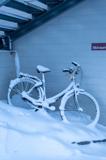 A vertical shot of a bike leaning against a building with a thick layer of snow on it