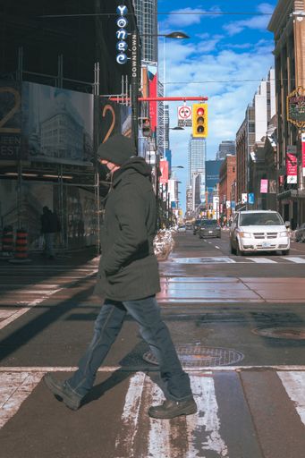 A male crossing the road street with cars and urban buildings against a blue sky in Toronto, Canada