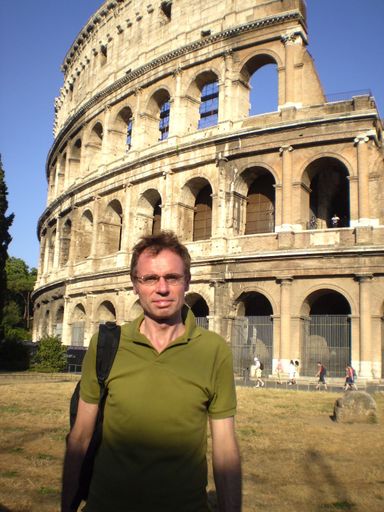 A vertical shot of a male wearing green top and eyeglasses standing near Colosseum in Rome, Italy