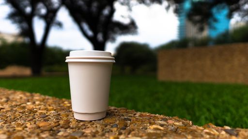 A closeup of a white paper coffee cup with space for text on a stone surface