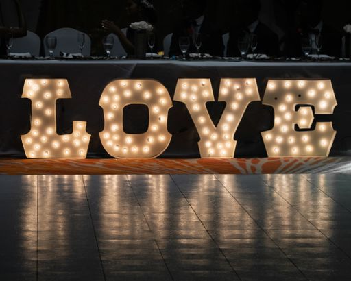 A closeup of a big shiny decoration "LOVE" in a restaurant with out of focus table and people sitting around it