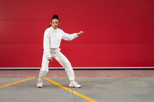 A Cheerful African American girl with long black hair dressed in sportswear listening to music with headphones on a red background