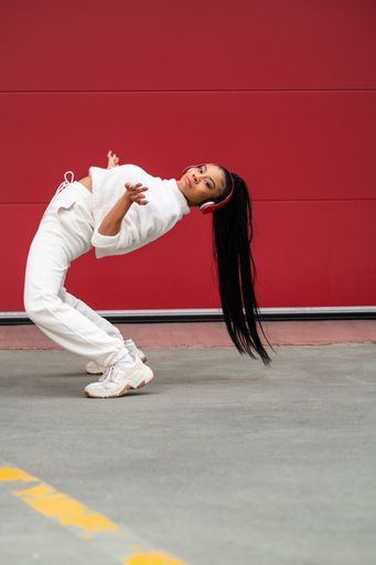 A Cheerful African American girl with long black hair dressed in sportswear listening to music with headphones on a red background