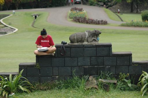 A close shot of a female sitting on a short rock wall near a statue with a blurred background
