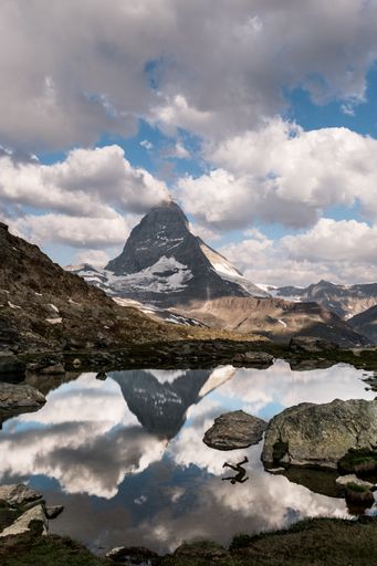 A beautiful vertical shot of a lake surrounded by mountains with a reflection of a person in the water