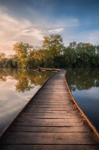 A vertical shot of a wooden bridge constructed on the water during the sunset