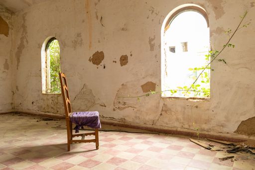A wooden chair in an old and abandoned room with a garden outdoors under the sunlight