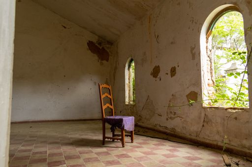 A wooden chair in an old and abandoned room with a garden outdoors under the sunlight