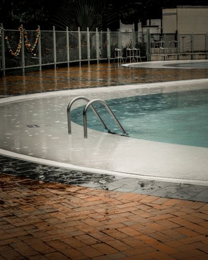 A vertical shot of an outdoor pool surrounded by orange bricks on a pouring rain