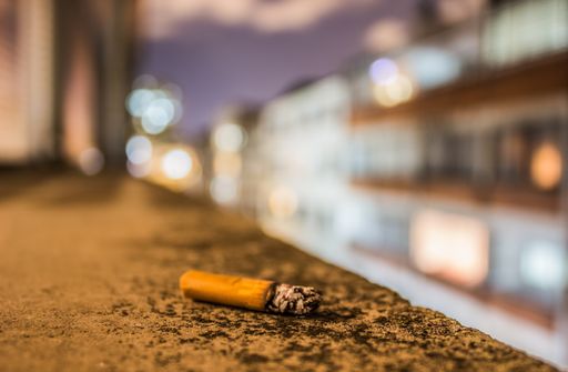 A closeup shot of a  cigarette stub on a stone surface and bokeh lights behind