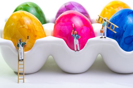 a team of painters with a wooden ladder and scaffolding is painting chicken eggs lying in a cup. White background