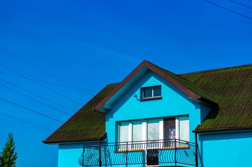 A low angle shot of a blue house with a green rooftop under a clear blue sky