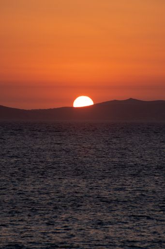 A vertical shot of the sun setting behind the hills at the sea
