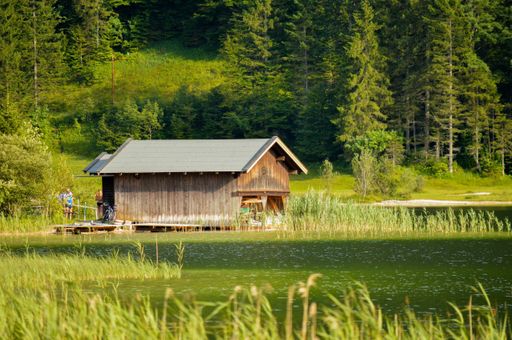 A beautiful shot of the small wooden house among green trees and along the lake