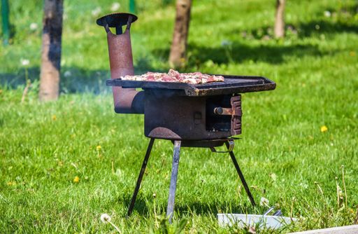 A selective focus shot of an old grill on the grass with meat on it