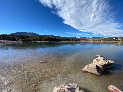 A scenic view of a lake with mountains against a cloudy blue sky on background