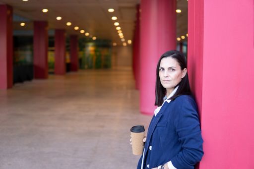 Beautiful Caucasian businesswoman with a cup of coffe looking at camera in the street outside of an office building