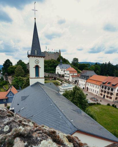 A vertical shot of a dome chapel near a roof around buildings and trees rising to the sky