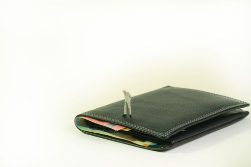 a businessman stands on a black purse, wallet where banknotes look out. isolated on white background, copy space