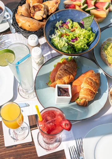 A top view of a breakfast with croissants, vegetable salad, lemonade, orange juice and strawberry smoothie